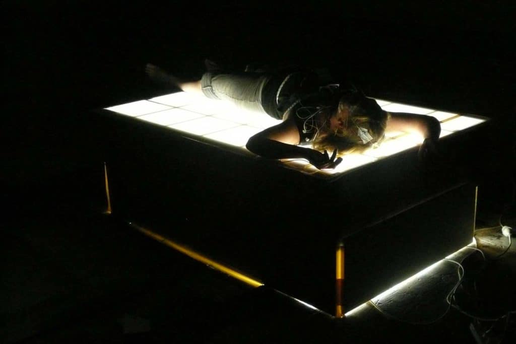 Riposo a turni. Una Light therapy box luminosa costruita come un letto per sperimentare le posizioni del sonno. <em>The Waking Incubator: scienza del sonno e arti dello spettacolo in dialogo</em>, Massey University NZ (2010). C. Brown, performer con EEG.